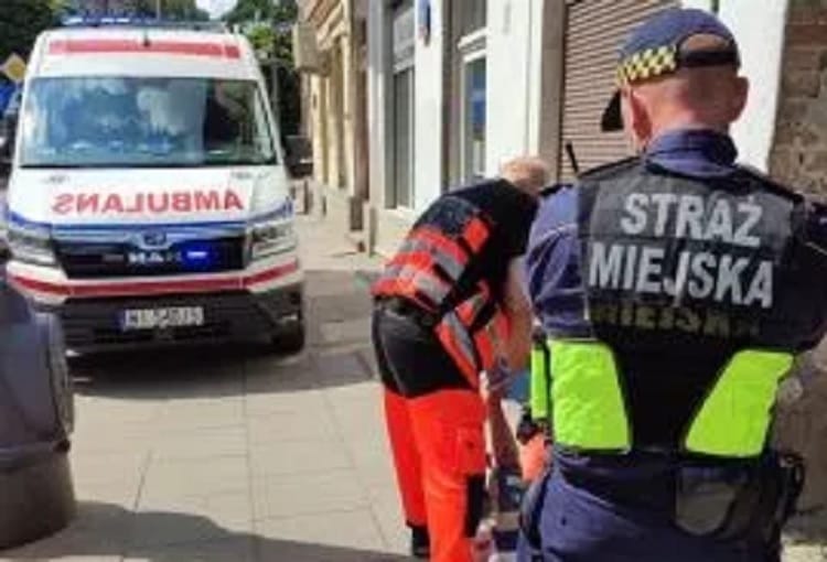 Ratownicy medyczni udzielają pomocy osobie znajdującej się w pobliżu karetki pogotowia i policjanta.