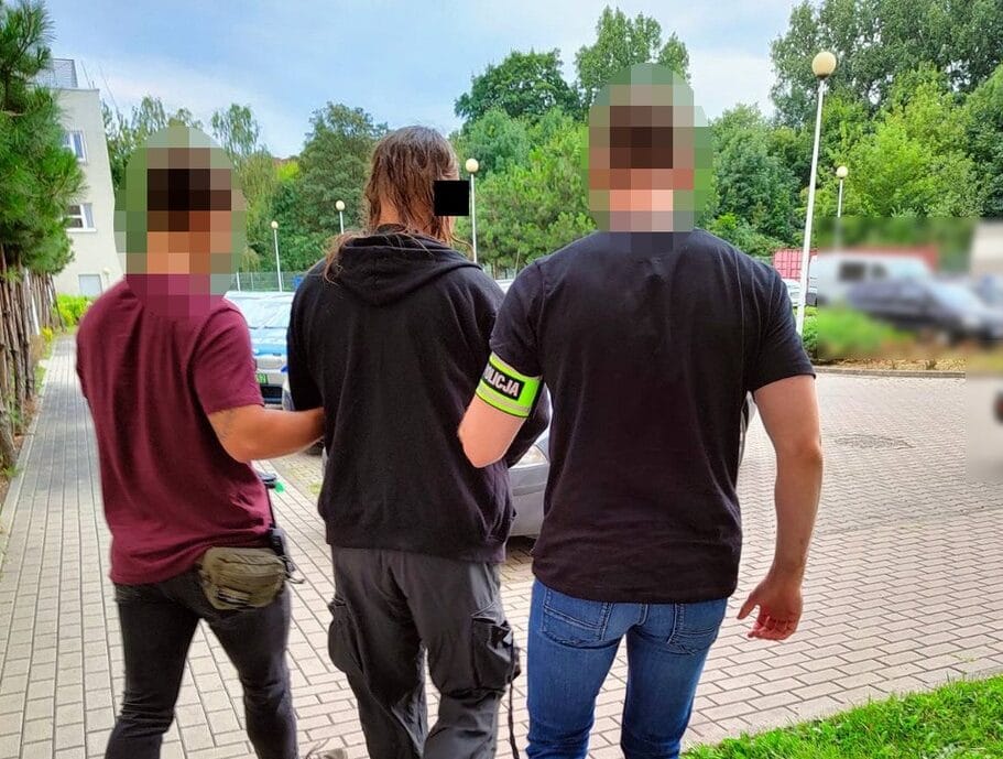 Policjanci eskortują dwóch podejrzanych w kajdankach.