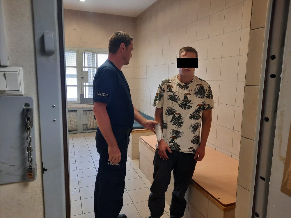 Policjant pomaga rannemu podejrzanemu w celi.