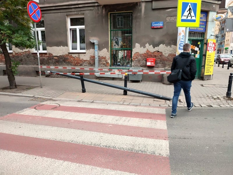 Złamany słup latarni ulicznej na przejściu dla pieszych. Mężczyzna przechodzi obok.