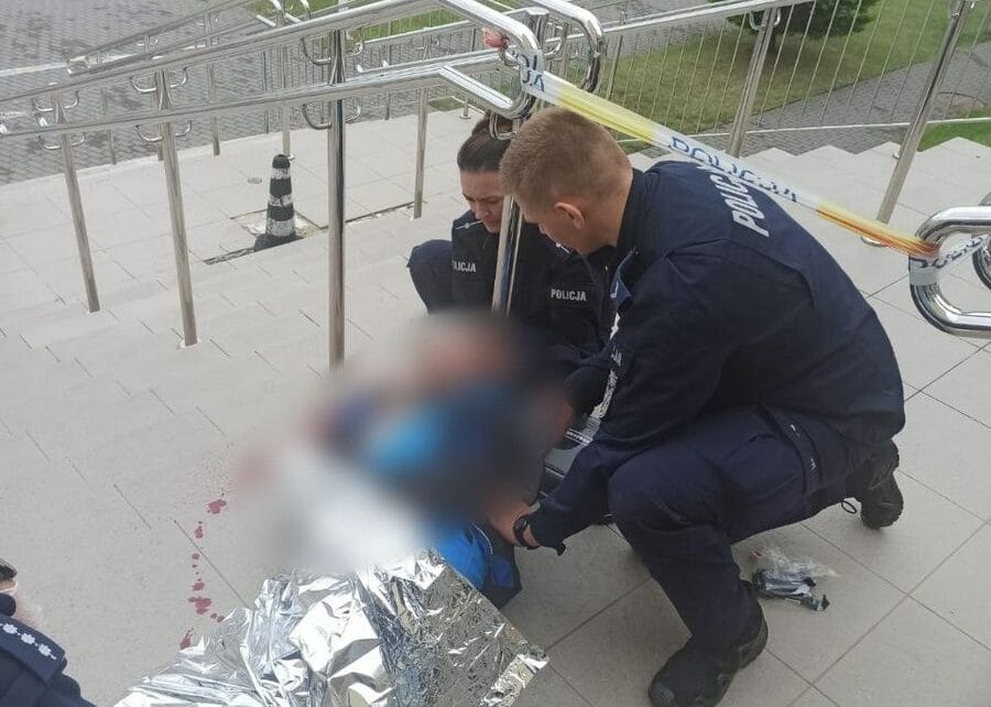 Policjanci udzielający pomocy rannej osobie na schodach. Widoczna krew.