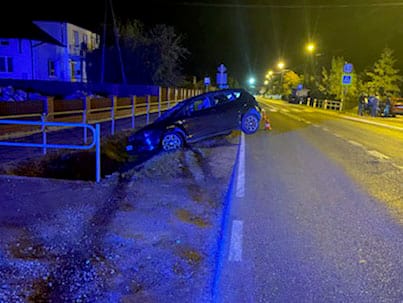 Wypadek samochodowy w nocy, pojazd leży na boku w rowie.