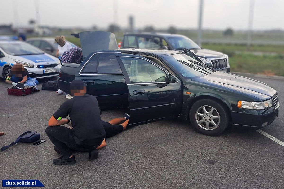 Policjanci pomagają rannemu w pobliżu ciemnego sedana na lotnisku