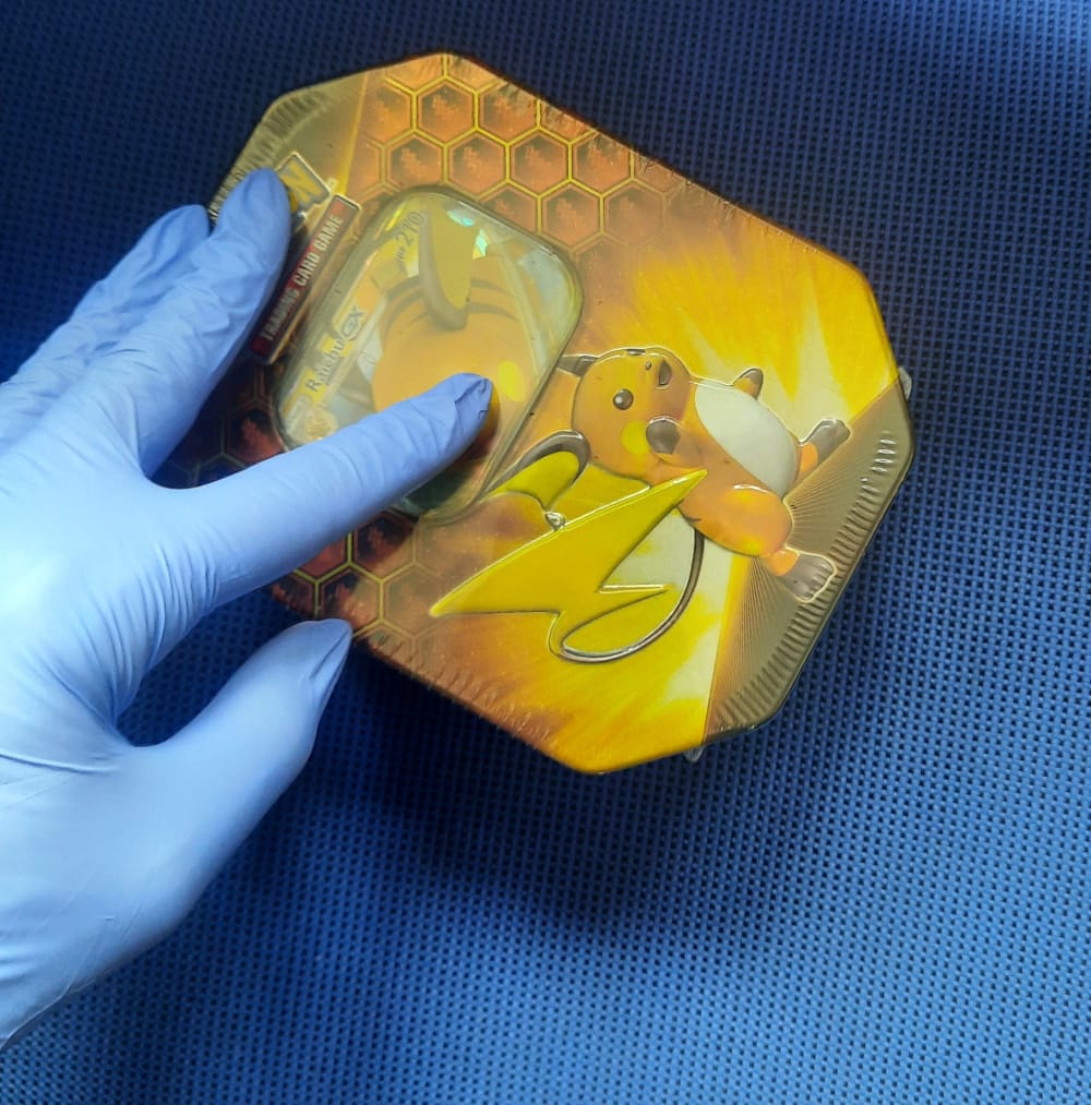 Dłoń w rękawiczce trzymająca puszkę Pokémonów Raichu GX z ilustracją Raichu i wzorem plastra miodu.