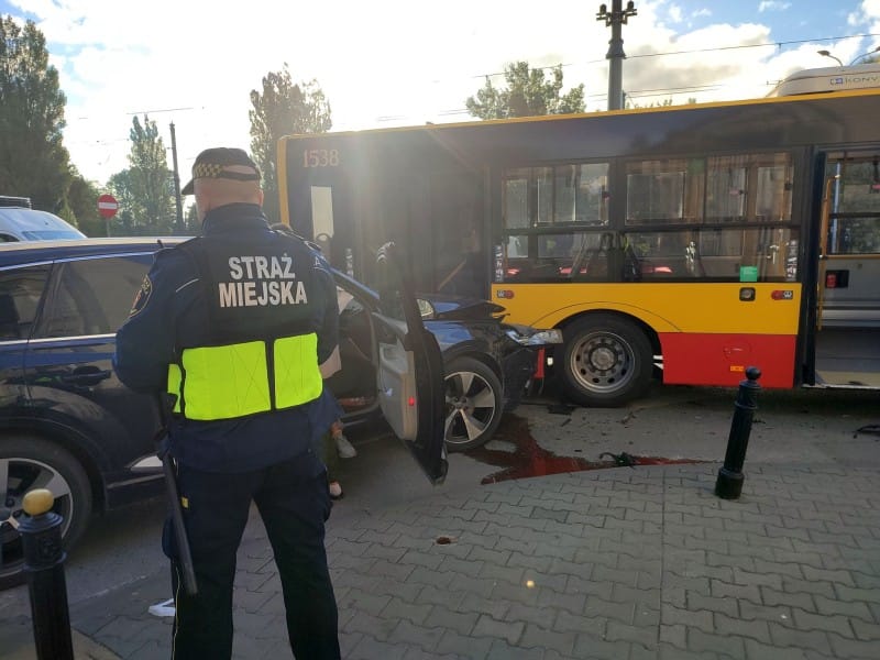 Policjant na miejscu wypadku z udziałem samochodu i autobusu. „Straż Miejska” widoczna na mundurze.