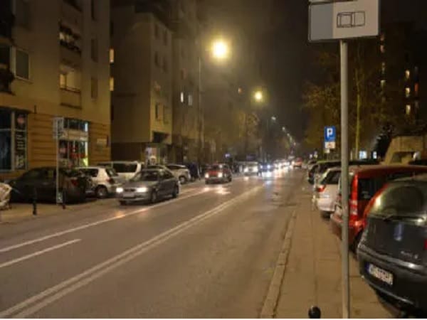 Nocny widok ulicy z zaparkowanymi samochodami i latarniami ulicznymi.