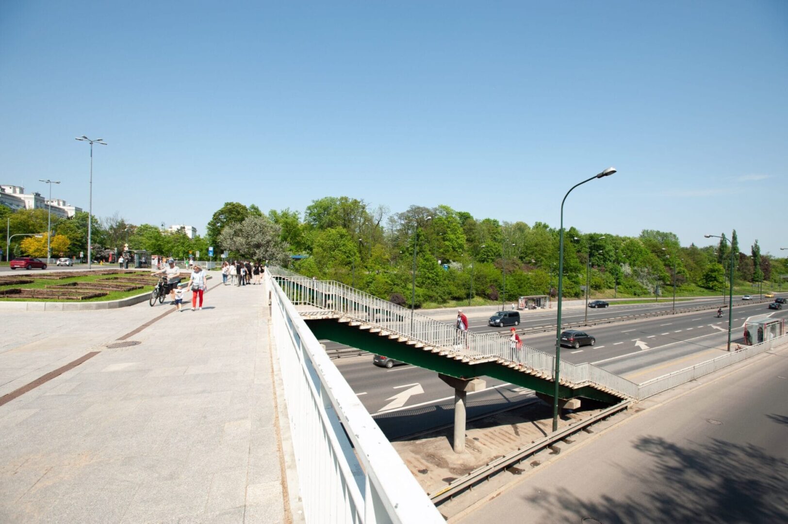 Kładka dla pieszych nad ulicą miejską, po której poruszają się piesi i samochody.