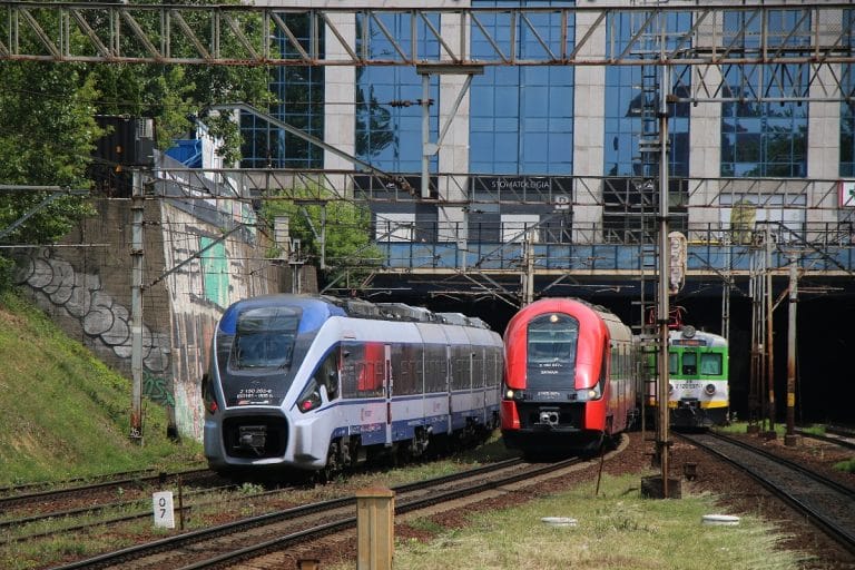 Dwa nowoczesne pociągi pasażerskie wjeżdżające na stację kolejową.