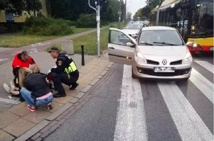 Ratownicy medyczni udzielają pomocy pieszemu rannemu w wypadku na przejściu dla pieszych w pobliżu Renault Clio.