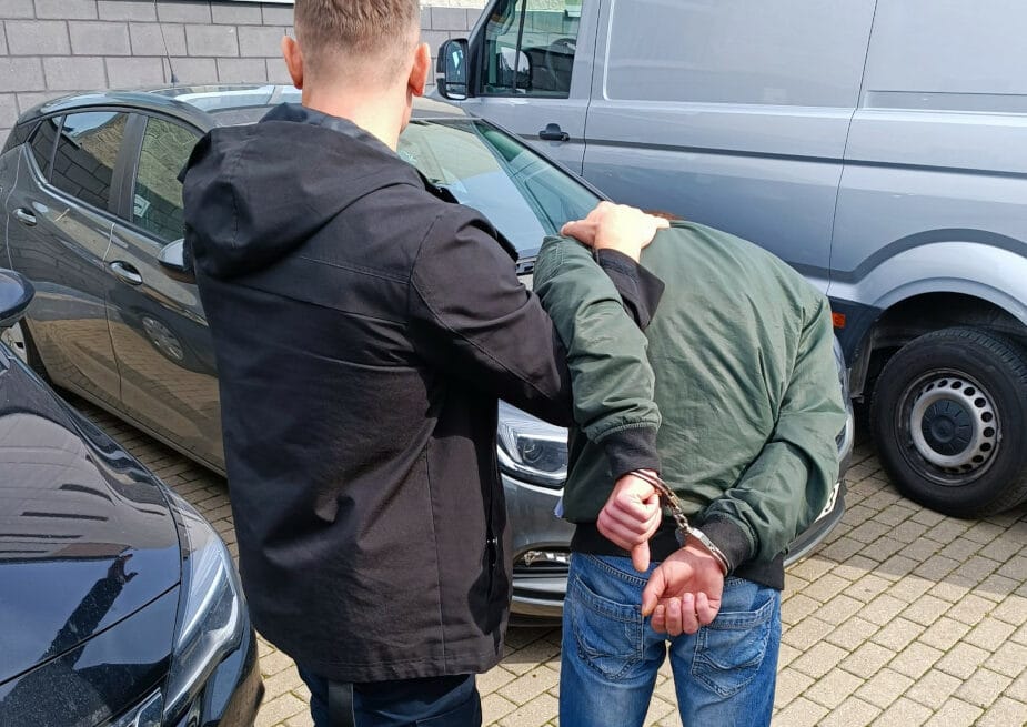 Policjant aresztujący podejrzanego w kajdankach.