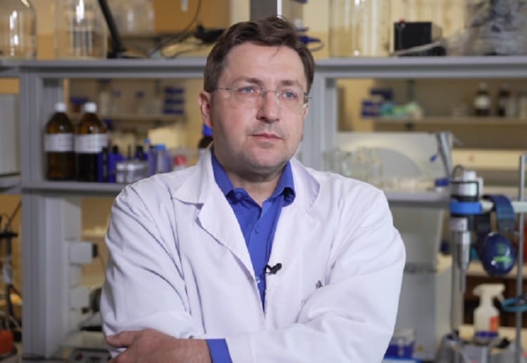 Naukowiec w fartuchu laboratoryjnym, ze skrzyżowanymi ramionami i zamyślonym wyrazem twarzy