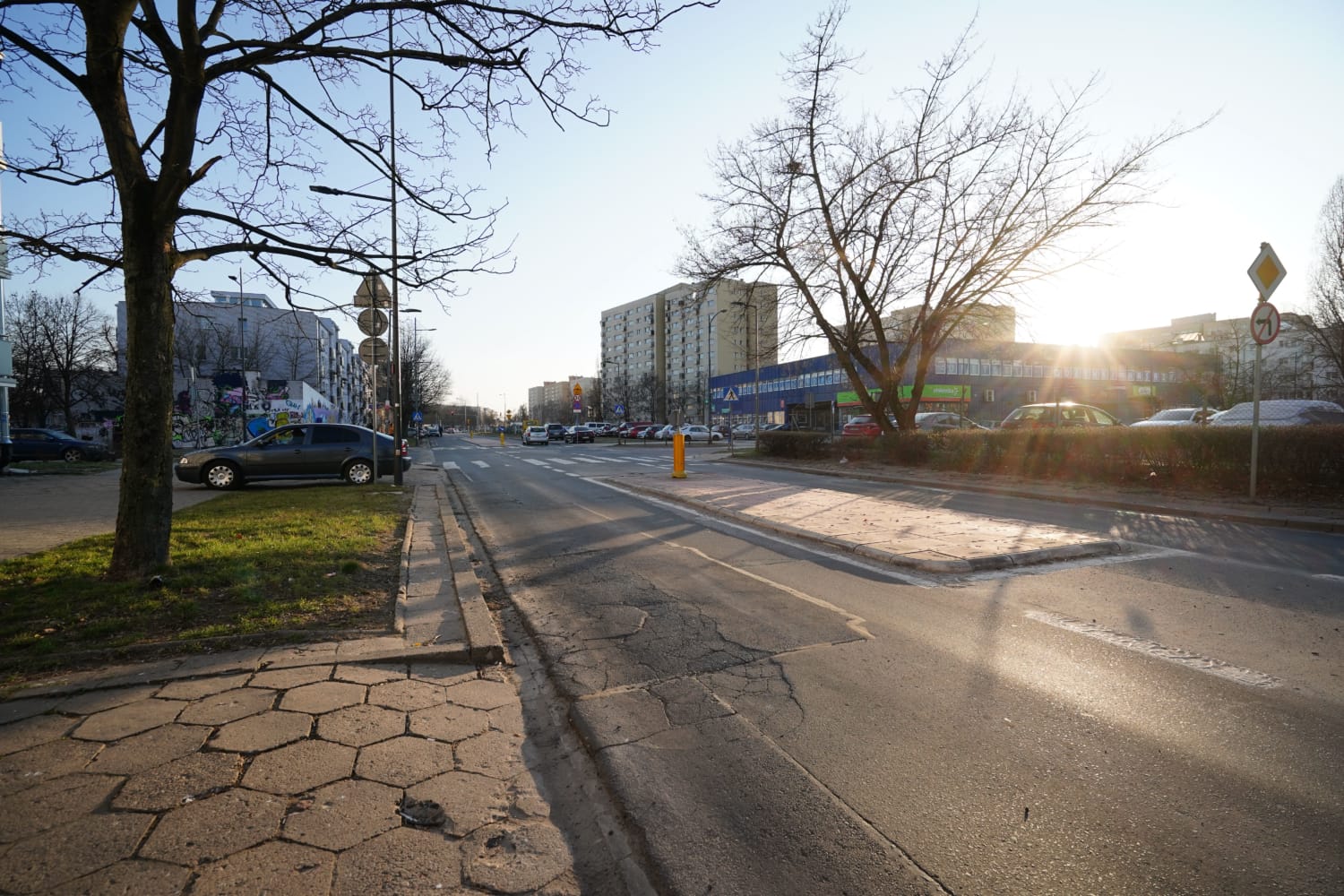 Pusta ulica miasta o zachodzie słońca, z zaparkowanymi samochodami i budynkami mieszkalnymi.