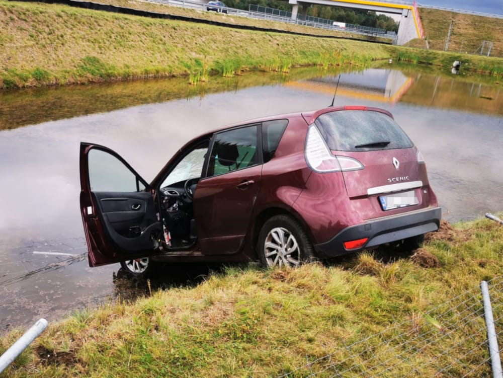 Bordowy Renault Scenic częściowo zatopiony w przydrożnym rowie.