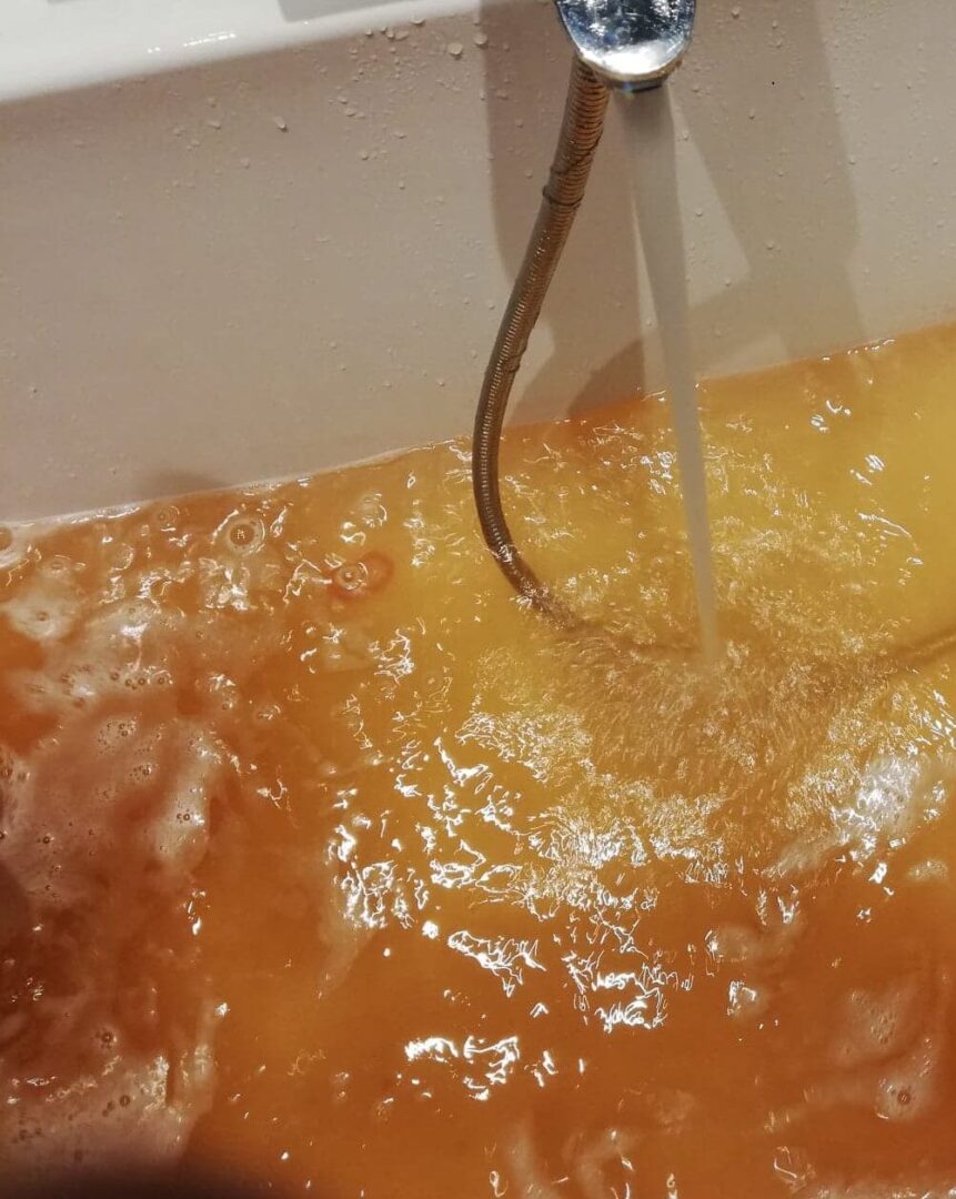 Brązowa, mętna woda wypełniająca wannę, z odkręconym kranem.