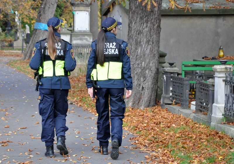 Dwie policjantki w mundurach patrolują cmentarz jesienią.