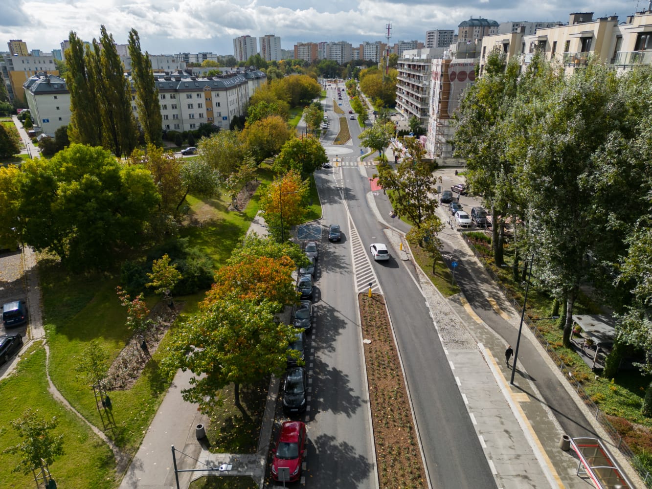 Widok z lotu ptaka na miejską ulicę z zielonymi przestrzeniami i zaparkowanymi samochodami.