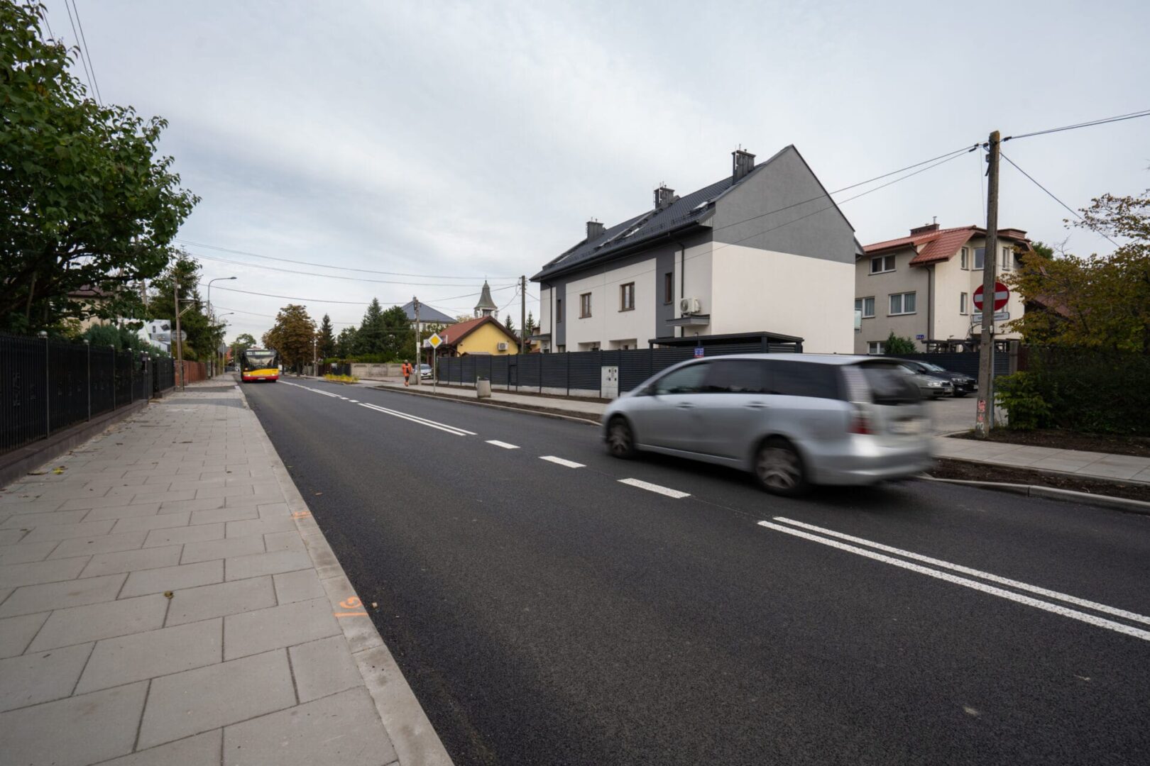 Spokojna ulica mieszkalna z nowymi domami i przejeżdżającymi samochodami.