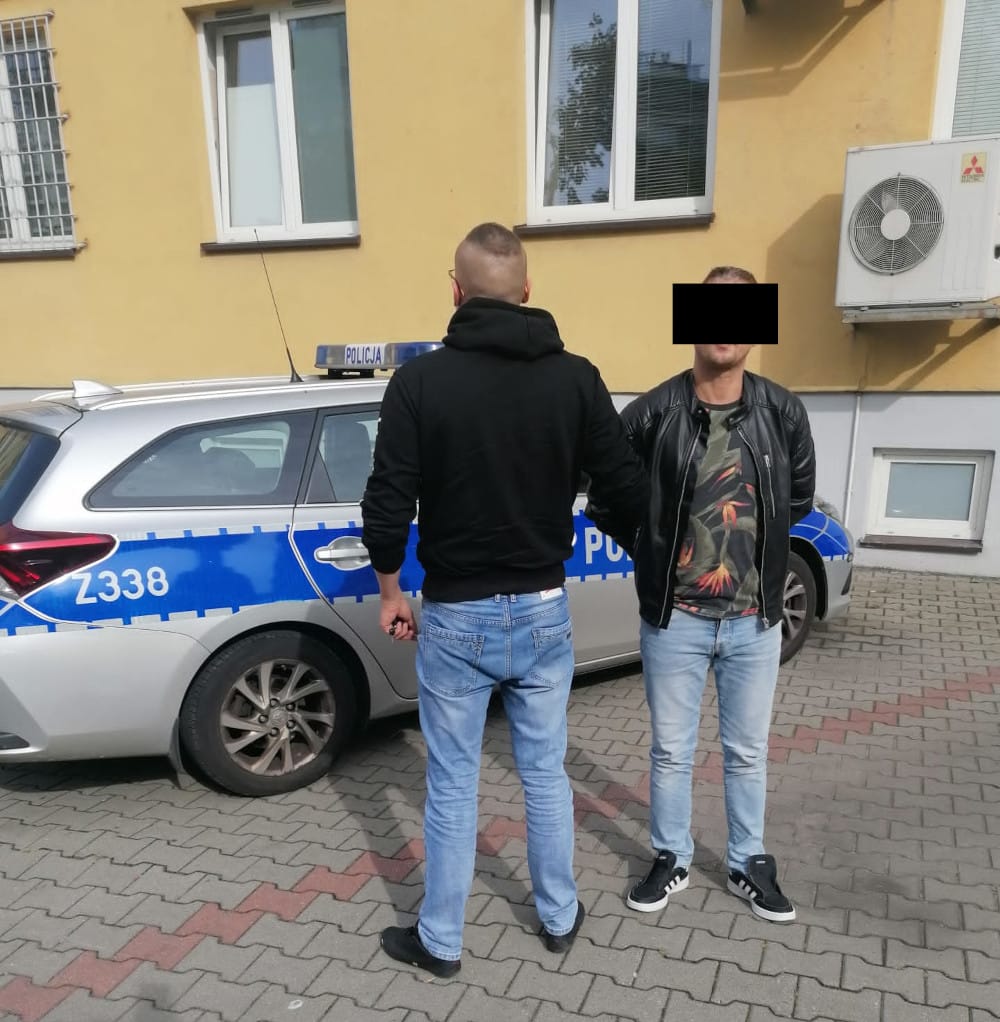 Dwóch mężczyzn w kajdankach stoi przy polskim radiowozie Z338.