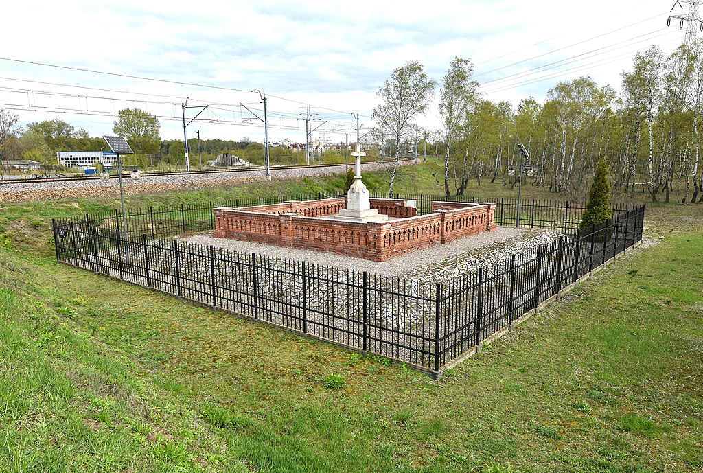 Pomnik murowany z krzyżem, ogrodzony, przy torach kolejowych