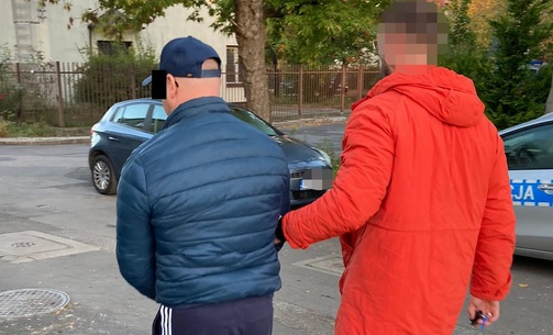Dwóch mężczyzn w kajdankach, jeden w niebieskiej kurtce, drugi w pomarańczowej. Aresztowanie przez policję.