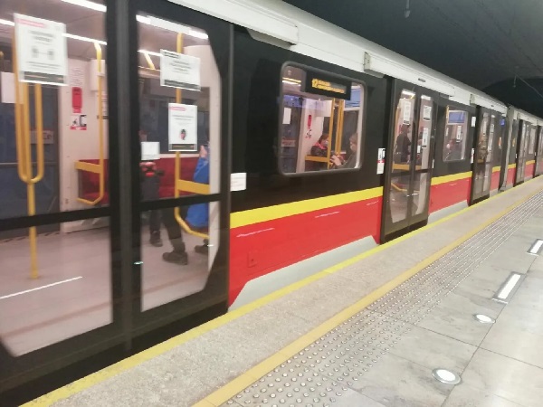 Pociąg metra warszawskiego zatrzymał się na peronie, pasażerowie widoczni przez okna.