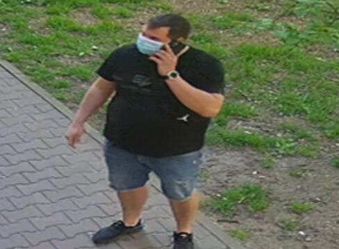 Mężczyzna w masce na twarzy, rozmawiający przez telefon, idący chodnikiem.