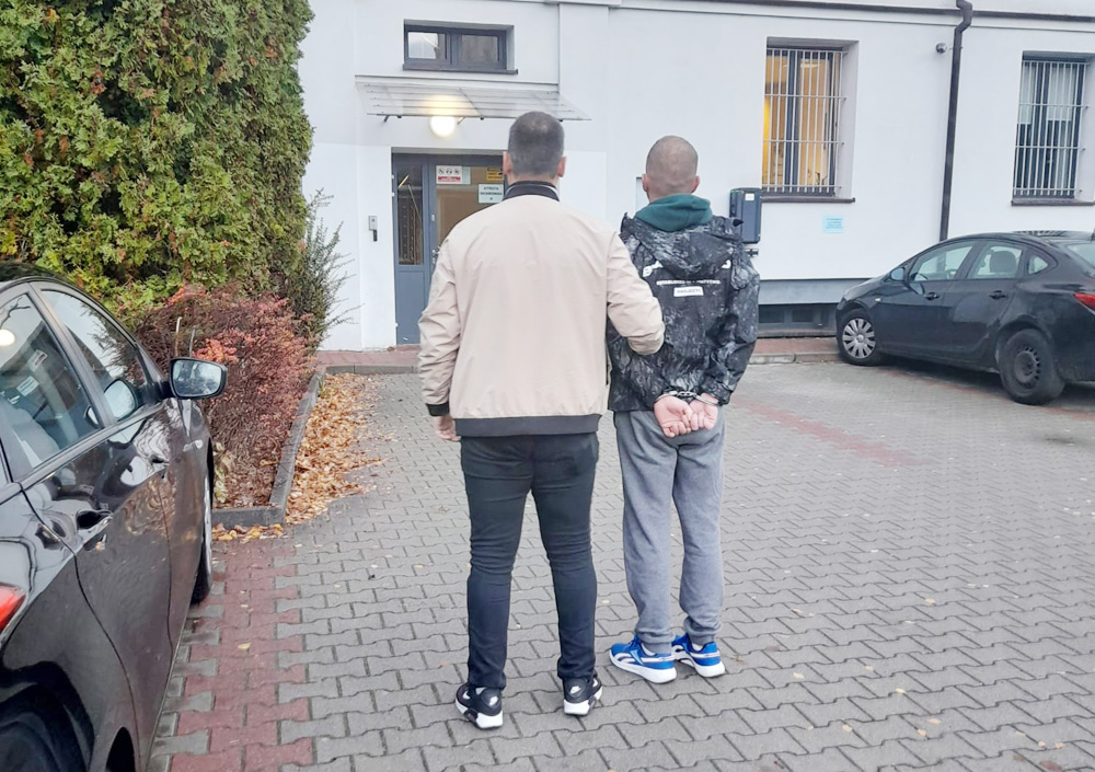 Policjant eskortujący skutego podejrzanego poza budynkiem.