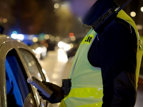 Policjant przeprowadzający badanie alkomatem przy drodze.