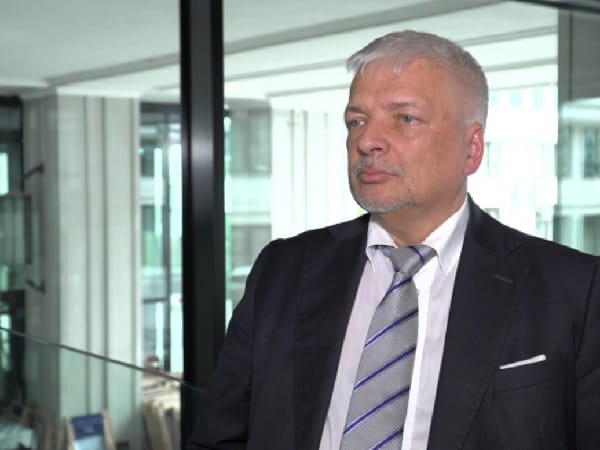 Portret mężczyzny w garniturze i krawacie, patrzącego zamyślonym wzrokiem.