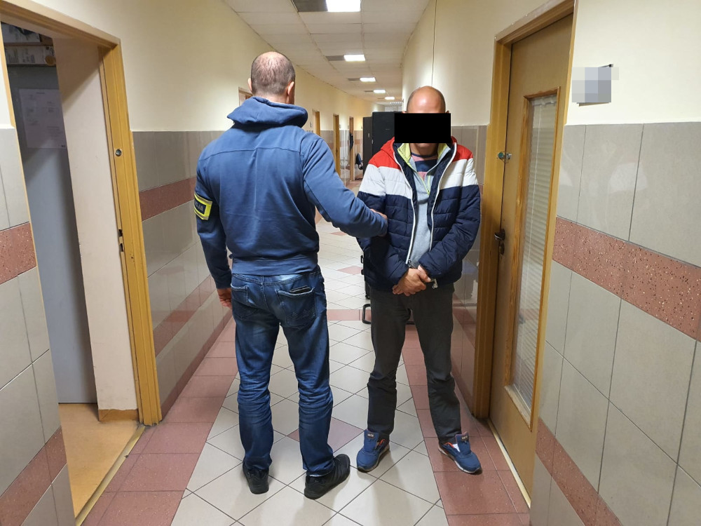 Policjant eskortujący podejrzanego korytarzem.