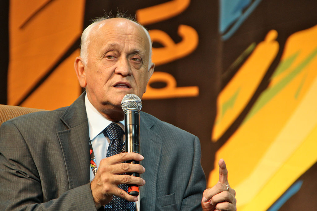 Starszy mężczyzna mówi do mikrofonu i gestykuluje ręką.