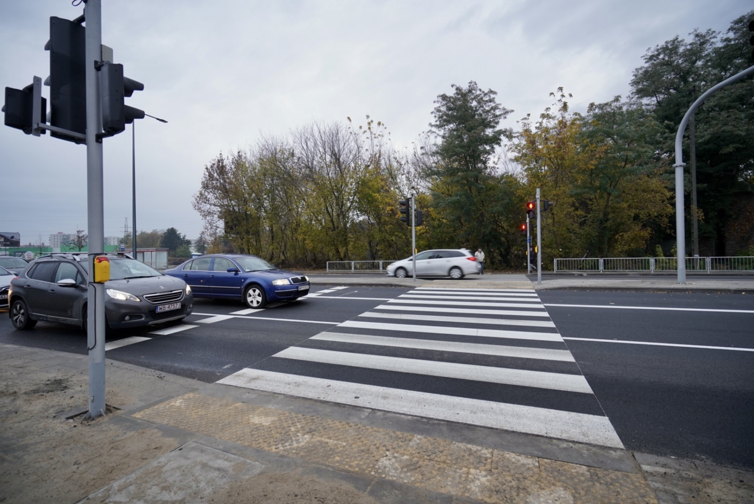 Samochody zatrzymujące się na przejściu dla pieszych z sygnalizacją świetlną. Bezpieczeństwo pieszych jest kluczowe.