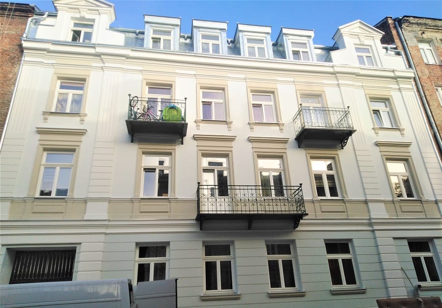 Odnowiony biały budynek mieszkalny z balkonami i ozdobnymi detalami