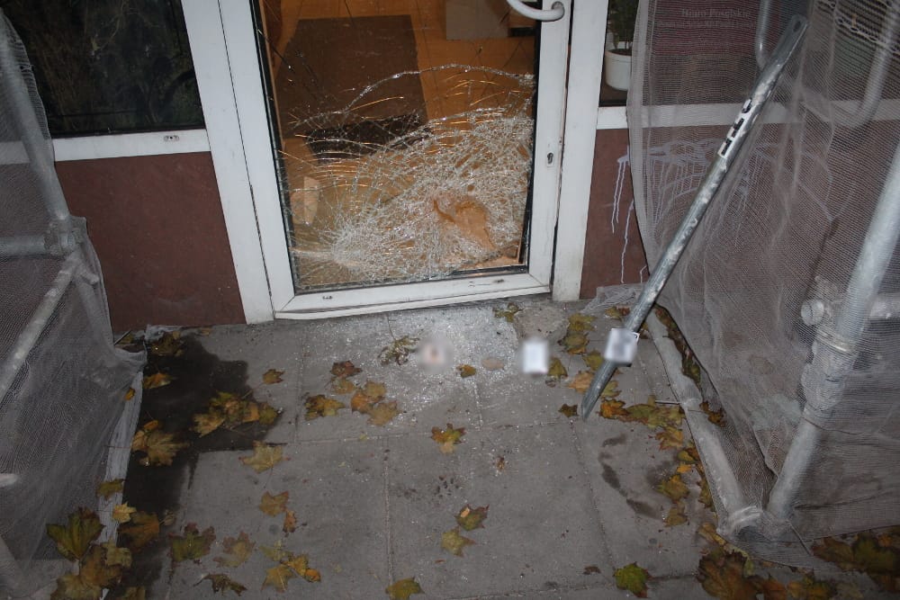 Zniszczona szyba sklepowa, na ziemi leżą potłuczone szkło i gruz.