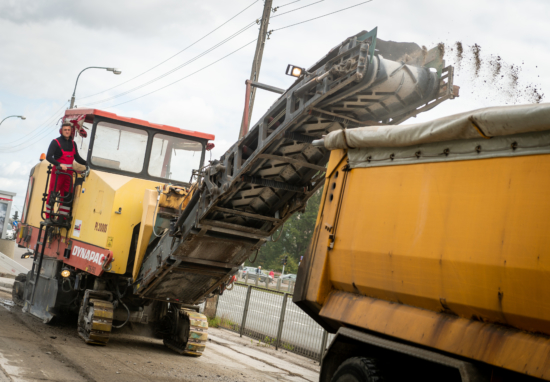 Operator frezarki drogowej ładuje frezowany asfalt do wywrotki.