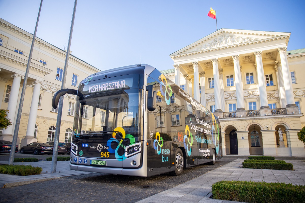 Nowoczesny autobus elektryczny MZA Warszawa zaparkowany przed zabytkowym budynkiem.