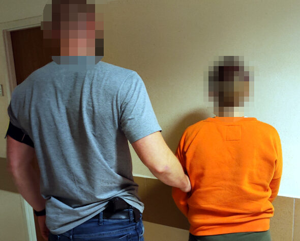 Policjant eskortujący nieletniego w pomarańczowym kombinezonie.