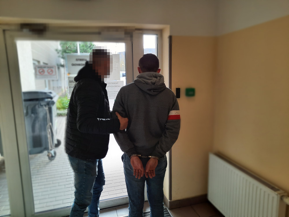 Policjant eskortujący podejrzanego w kajdankach przez drzwi