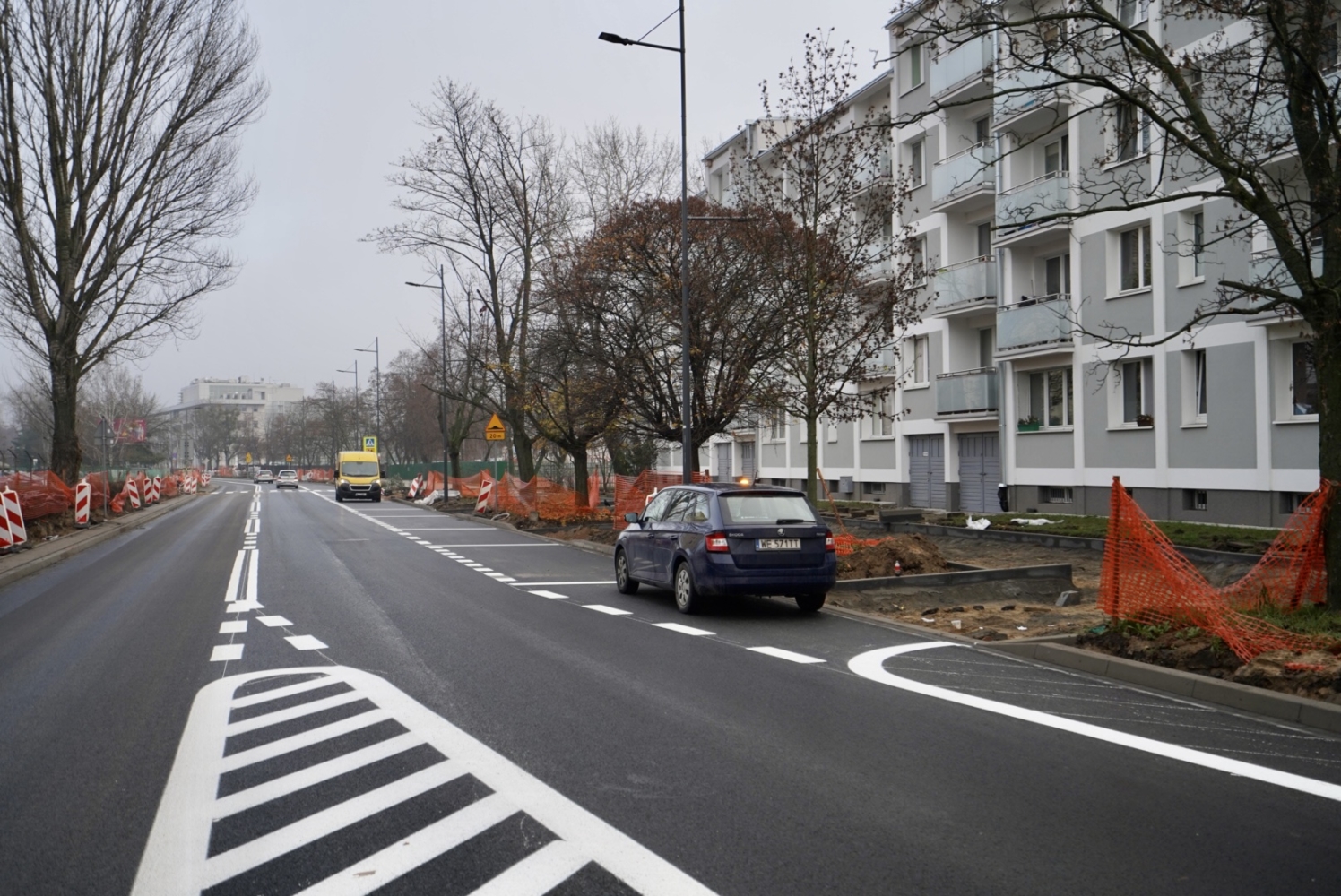 Nowo wyasfaltowana droga z zaparkowanym samochodem w pobliżu budynku mieszkalnego w trakcie budowy