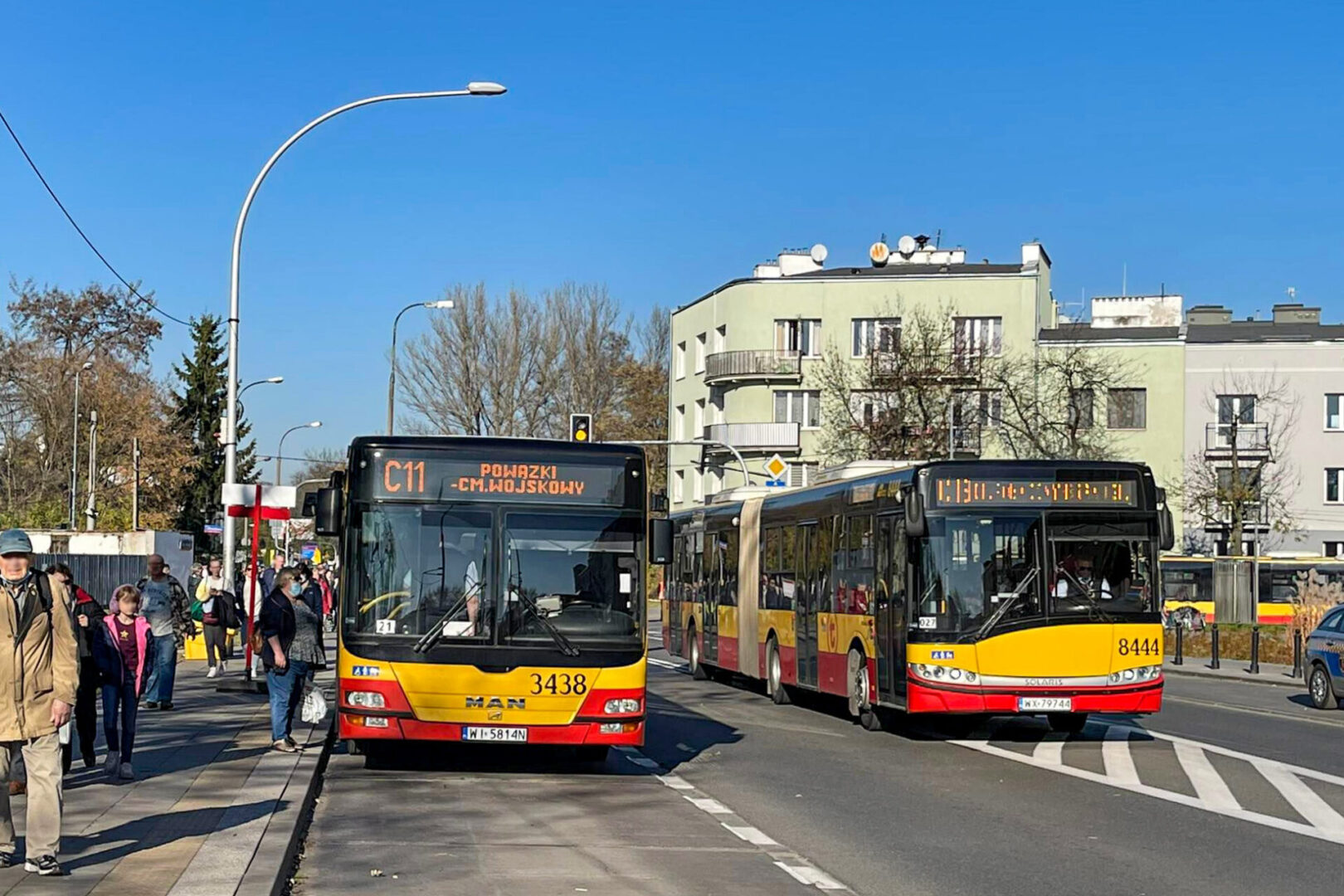 Dwa autobusy miejskie, numery 3438 i 8444, zatrzymały się na przystanku autobusowym. Wyświetlana jest trasa C11 do Powązki-Cm.Wojskowy.