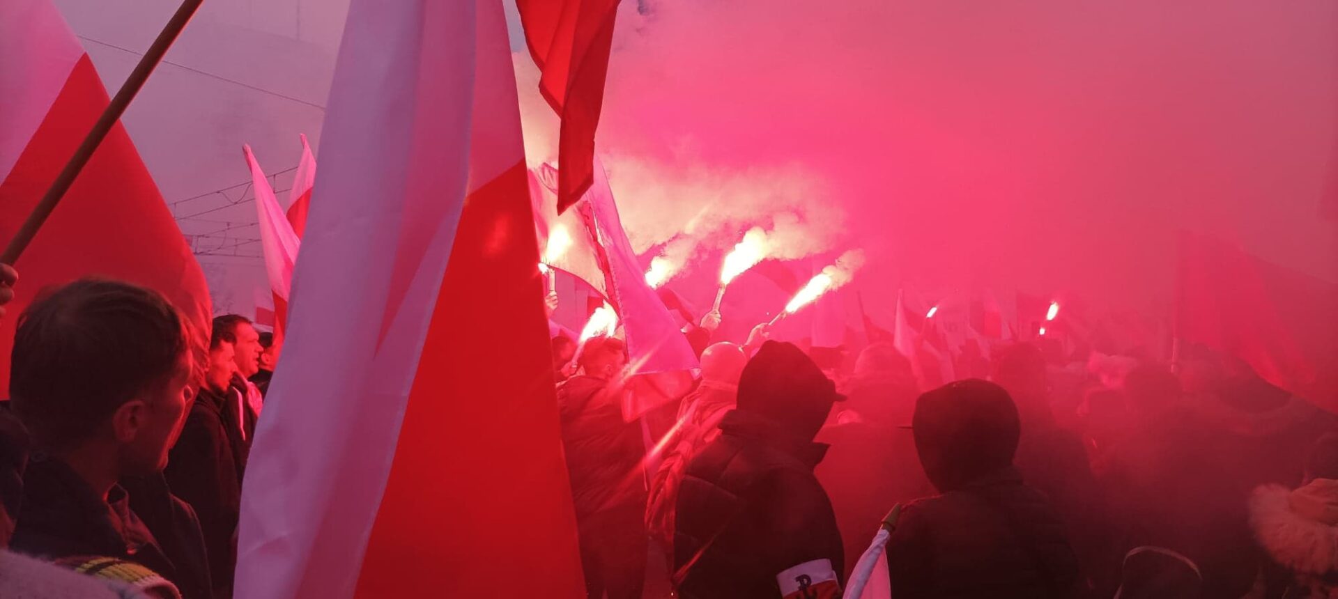 Protestujący machają polskimi flagami i czerwonymi racami podczas demonstracji.