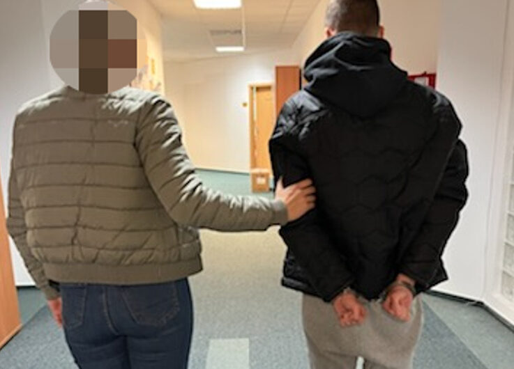 Policjant eskortujący podejrzanego w kajdankach korytarzem