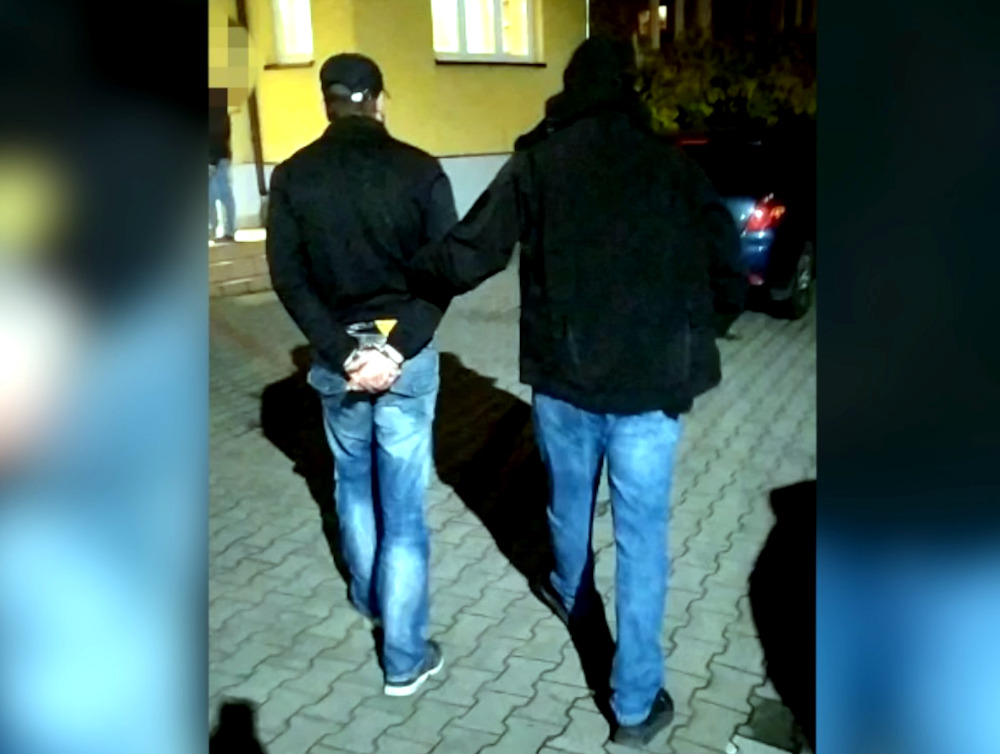 Dwóch mężczyzn w kajdankach, eskortowanych przez policję.