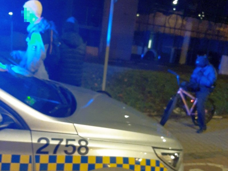 Policjanci rozmawiają z osobą na rowerze w nocy. Widoczny numer samochodu 2758.