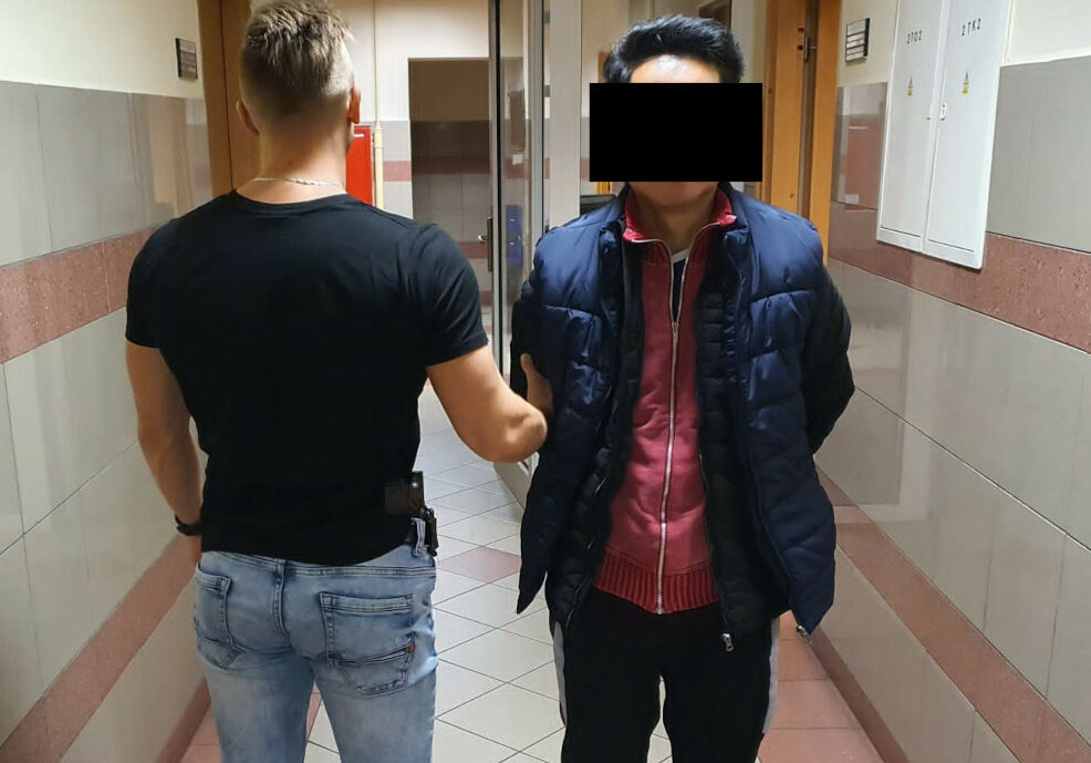 Policjant eskortujący podejrzanego korytarzem.