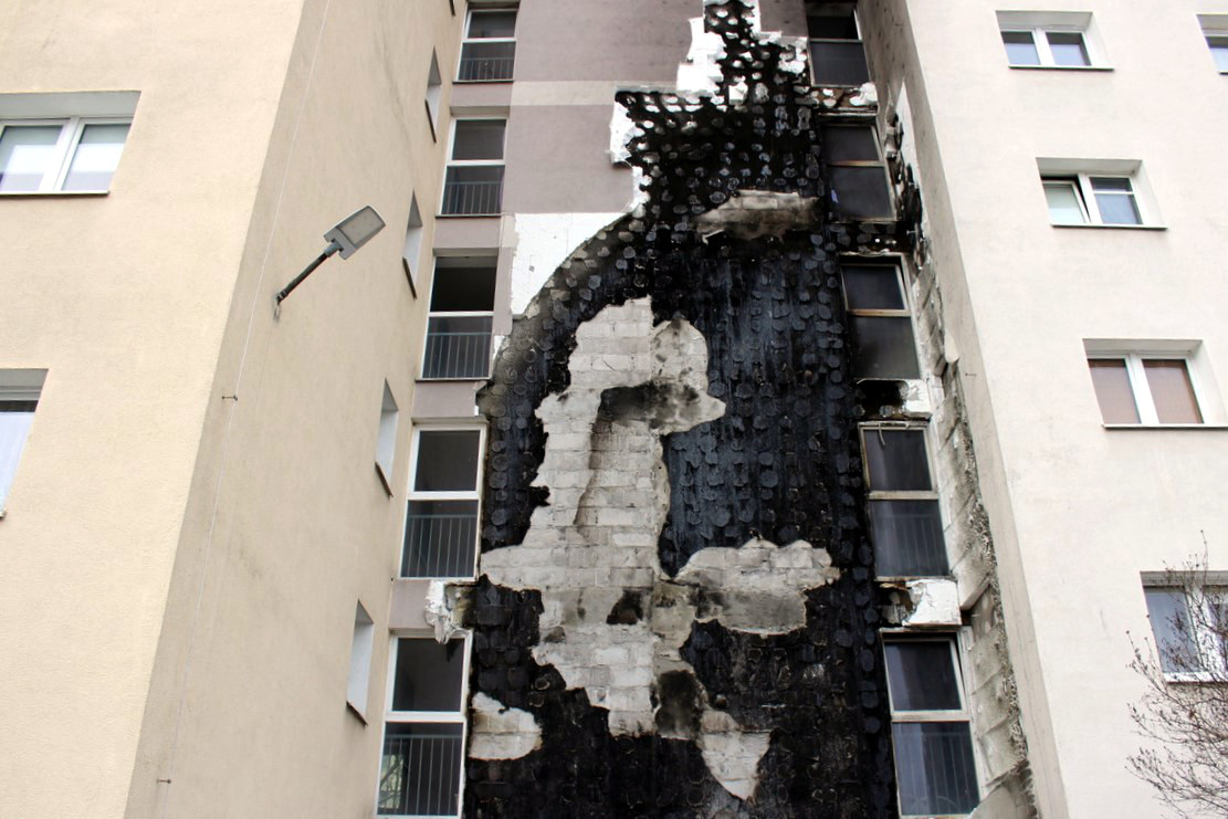 Elewacja budynku mieszkalnego zniszczona przez ogień, ze znacznym uszkodzeniem jednej ściany.