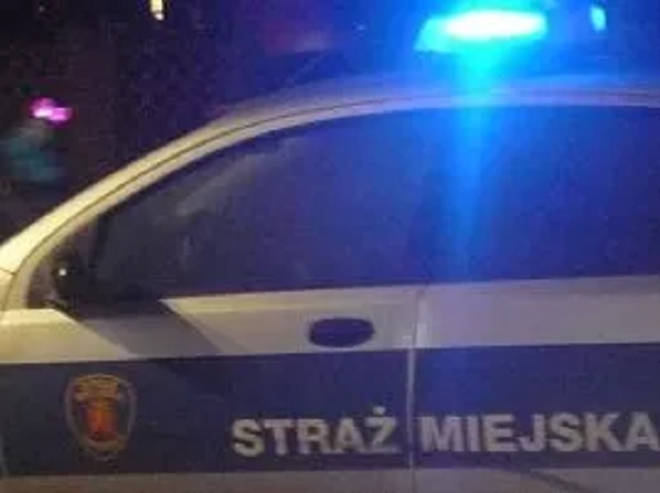 Radiowóz Straży Miejskiej z migającymi w nocy niebieskimi światłami.