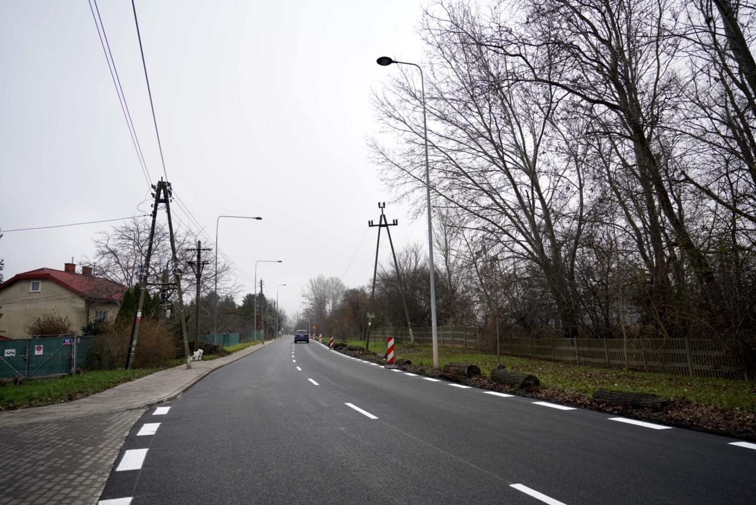 Pusta asfaltowa droga na obszarze wiejskim z drzewami i domem w tle.