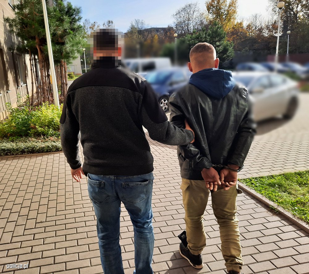 Policjant eskortujący podejrzanego w kajdankach