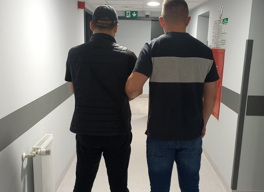 Dwóch mężczyzn idzie korytarzem, jeden z nich trzyma rękę na ramieniu drugiego.